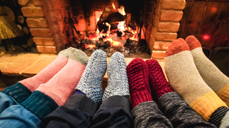 Legs view of happy family wearing warm socks in front of cozy fireplace - Focus on left socks.