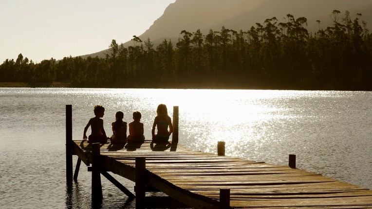 Children sitting on a dock by a lake